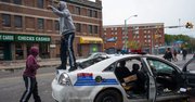 Personas gritan sobre un vehículo de la policía abandonado que fue atacado durante protestas luego del funeral de Freddie Gray hoy, lunes 27 de abril de 2015, en Baltimore 