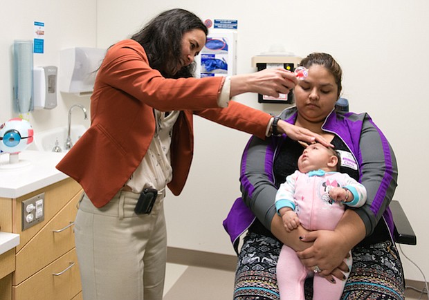Aryanna Guadalupe Sánchez-Ríos se sienta en la falda de su tía Jessica Ríos. Micahel Cabrera, oftalmóloga pediátrica en el Hospital de Niños de Seattle, utiliza un juguete para llamar la atención del bebé durante su examen ocular el 5 de mayo de 2017.