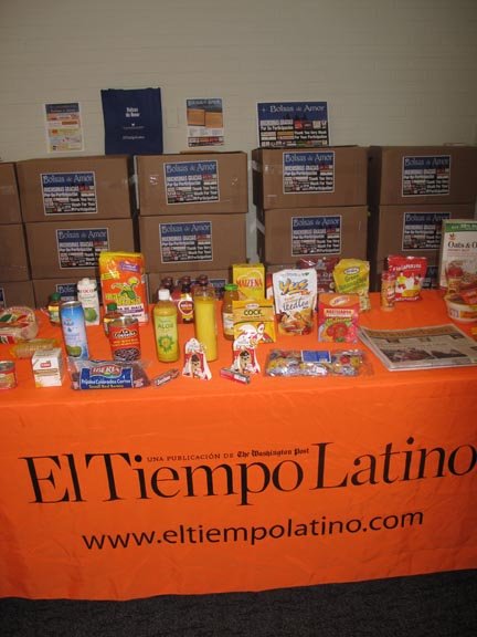En la mesa, se mostraron los productos de EMD SALES, algunos de los cuales formaron parte de las cajas entregadas. Atrás, las cajas esperan por las familias.