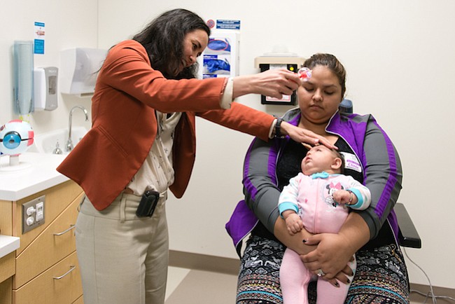 Aryanna Guadalupe Sánchez-Ríos se sienta en la falda de su tía Jessica Ríos. Micahel Cabrera, oftalmóloga pediátrica en el Hospital de Niños de Seattle, utiliza un juguete para llamar la atención del bebé durante su examen ocular el 5 de mayo de 2017.