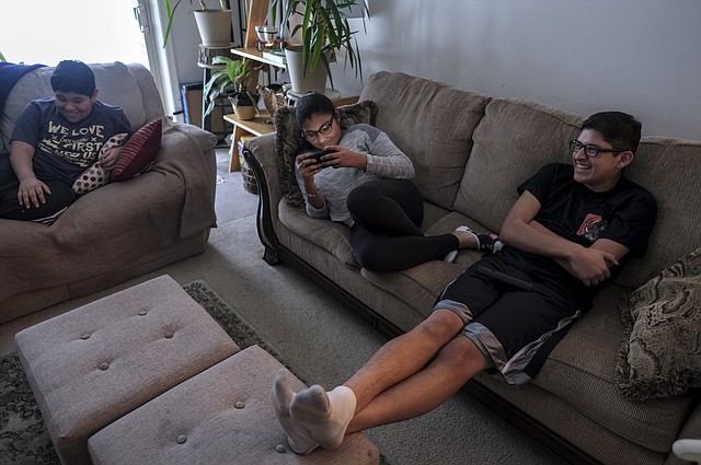 Los hermanos Martínez, Emilio, de 11, Miranda, de 12 y Adolfo, de 16, a la derecha, ven un programa de comedias en la televisión en su casa en Owings Mills, Maryland.