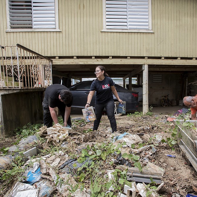 El hombre con camisa naranja está ayudando a limpiar la casa de su hermano. Voluntarios de Mentes Puertorriqueñas en Acción (camisa azul) participan en la labor.