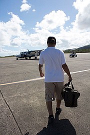 Joe García camina por la pista para tomar el avión que lo llevará a Vieques. Lleva vendas en su brazo porque acaba de terminar su diálisis.
