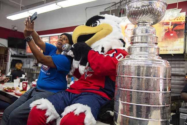 TROFEO. Una fan de los Washington Capitals se toma una selfie con la Stanley Cup y la mascota Slapshot durante una gira del trofeo en Ben's Chili Bowl antes del primer partido de la temporada el miércoles por la noche en Washington, DC.