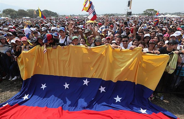 Un grupo de personas sostiene una gran bandera venezolana durante el concierto Venezuela Aid Live.