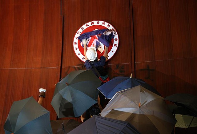 PROTESTAS. Un manifestante coloca una bandera británica sobre el emblema de Hong Kong tras irrumpir en la sede del Parlamento, este lunes en Hong Kong