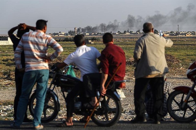 CONFLICTO. Varias personas observan la frontera turco-siria mientras el humo se eleva desde objetivos dentro de Siria. Vista desde el distrito de Akcakale en Sanliurfa, Turquía, el 13 de octubre de 2019. | Foto: Efe.