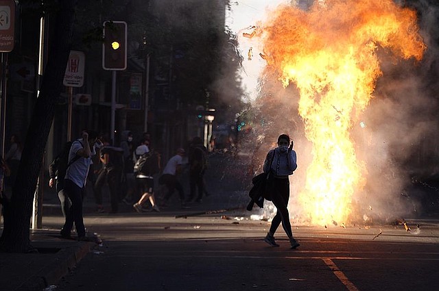 PROTESTAS. Una barricada estalla según pasa una joven cerca de ella durante una protesta contra el Gobierno de Sebastián Piñera este lunes, por décimo día consecutivo en las calles de Santiago