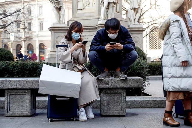 CONTAGIO. Dos turistas asiáticos con máscaras protectoras revisan sus smartphones en el área central de Milán, Italia, 24 de febrero de 2020