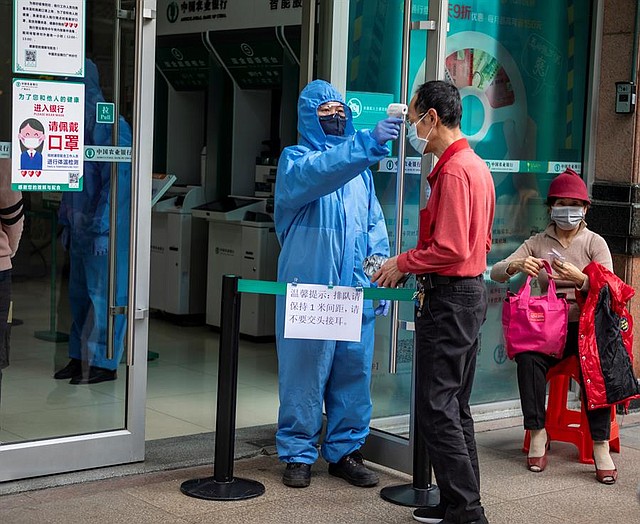ENFERMEDAD. Un guardia de seguridad con máscara y equipo de protección mide la temperatura corporal de los visitantes a la entrada de un banco en Guangzhou, provincia de Guangdong, China, 24 de febrero de 2020