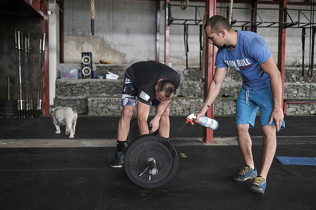 PREVENCIÓN. Un hombre aplica desinfectante a los discos de una pesa mientras entrena junto con otro deportista en un gimnasio, el viernes 1° de mayo, luego de que algunos negocios empezarán una apertura paulatina en San José (Costa Rica). | Foto: Efe/Jeffrey Arguedas.
