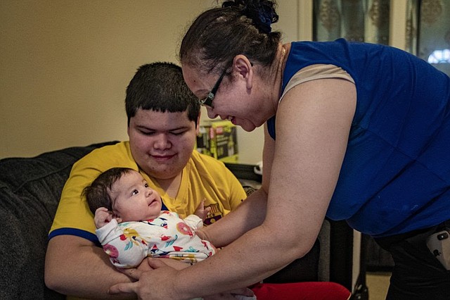 Carolina toma a su bebé de 4 meses de los brazos de su hijo. (Jesse Costa / WBUR)