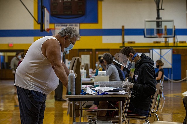 VOTANTES. Un votante se registra para recibir su boleta en el colegio electoral del Distrito 1 de la Escuela Secundaria de East Boston al comenzar el día de las elecciones