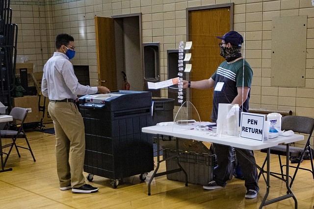 RESTRICCIONES. Los trabajadores electorales de la Secundaria Brookline introducen las boletas de votación anticipada del precinto 6 en una máquina de votación