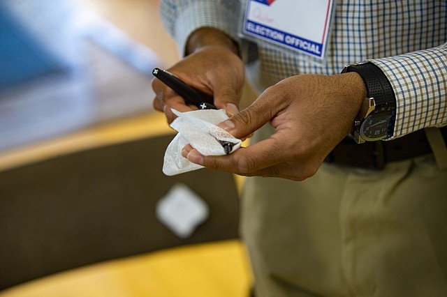 PRECAUCIÓN. Un trabajador electoral desinfecta los bolígrafos usados por los votantes para marcar sus boletas en la Secundaria Brookline